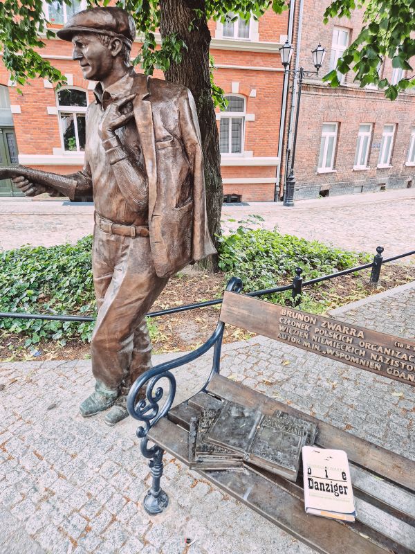 Bronon Zwarra-Staute und Bank aus Bronze in seiner Geburtsstraße in Danzig mit einem Exemplar von "Die Danziger".